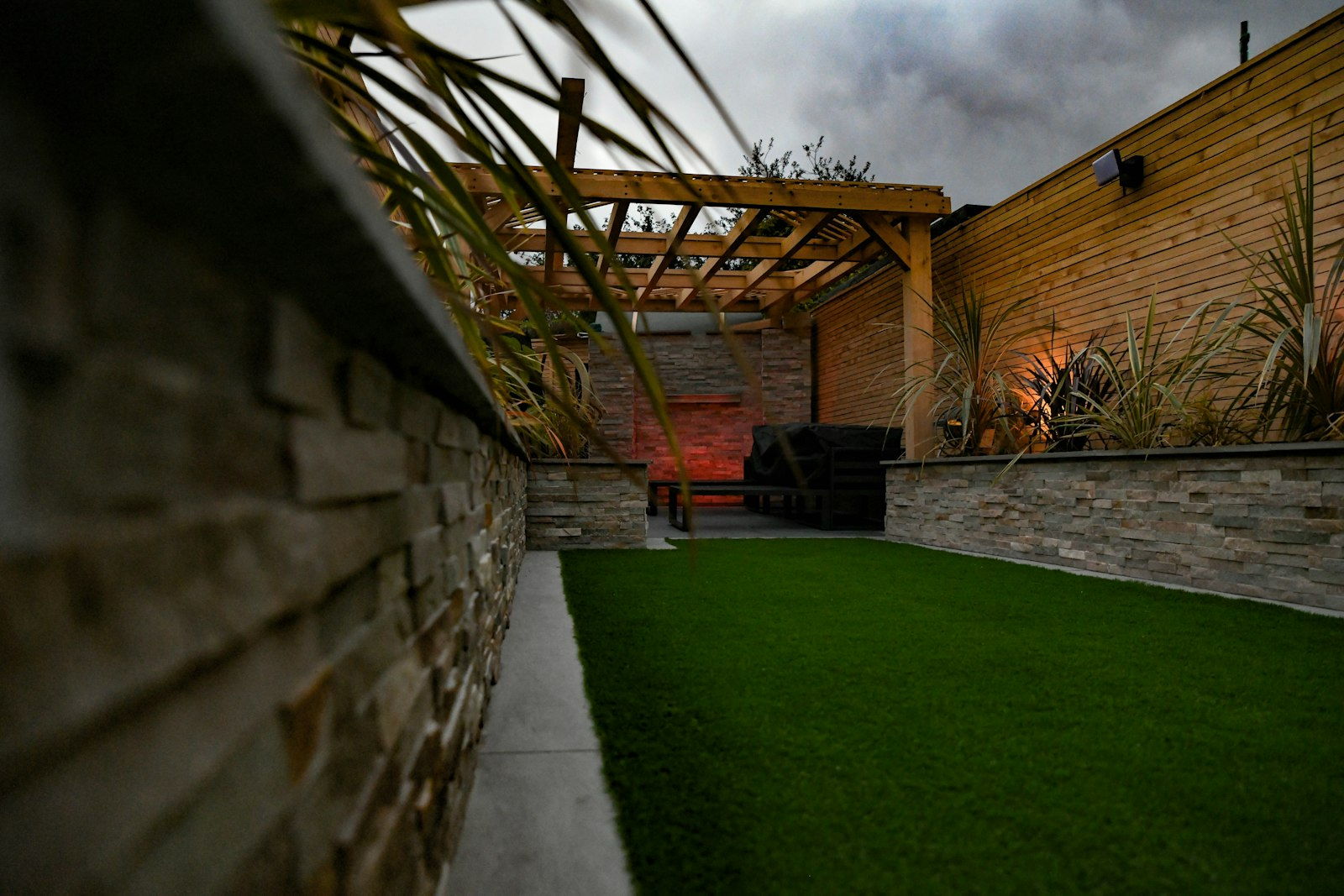 Stacked stone wall beside an artificial turf lawn with a timber shade structure